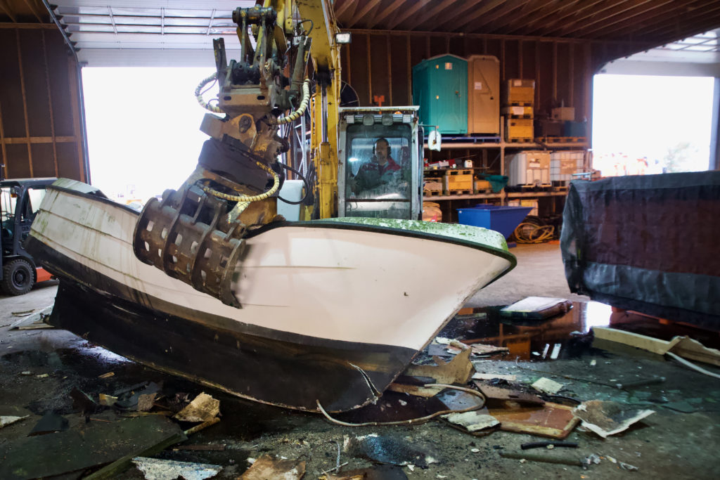 Glenn Erik Østhassel knuser den gamle fiskebåten med gravemaskinen, men plukker ut alt som kan gjenvinnes.